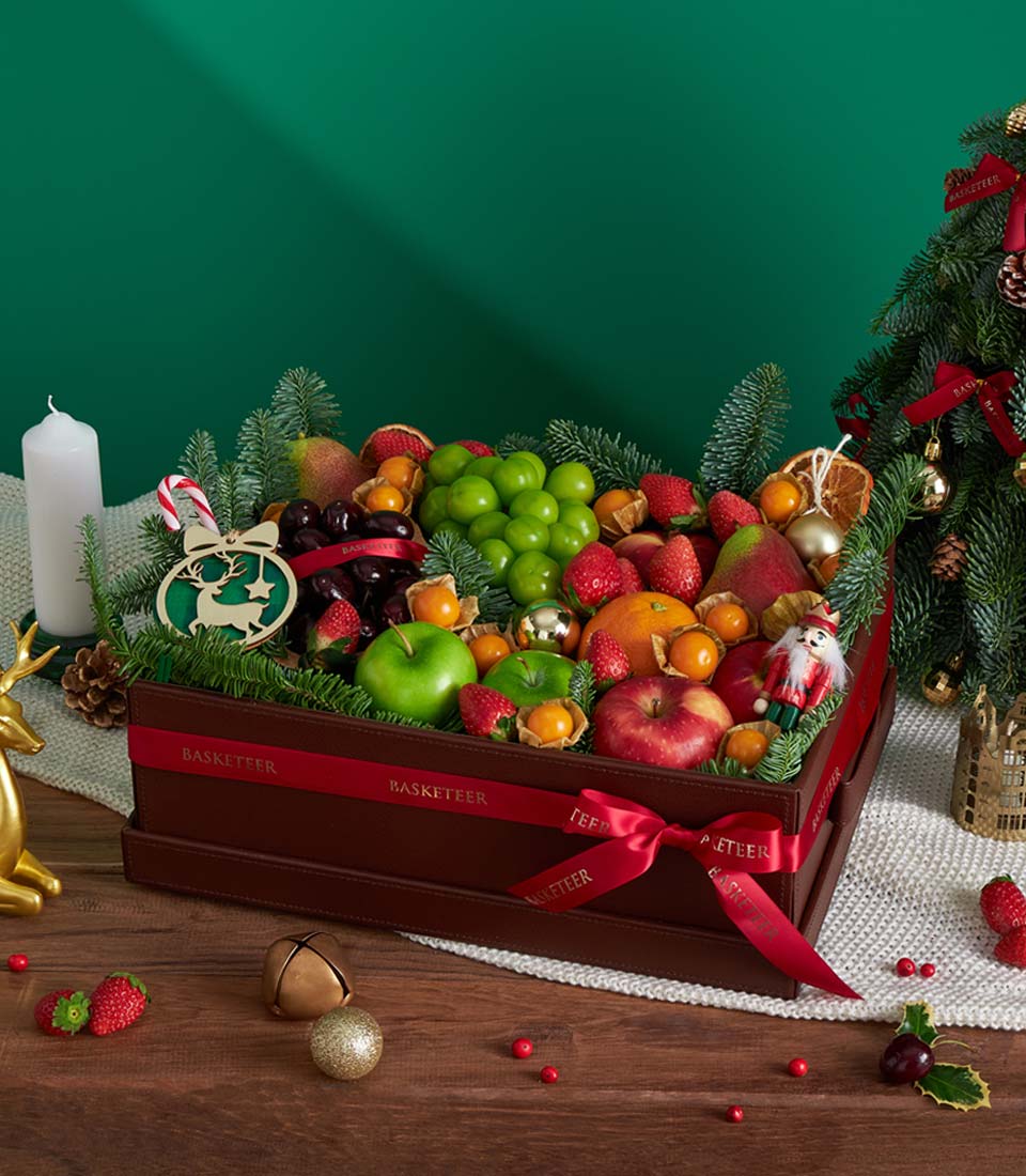 Festive Christmas fruit basket with fresh apples, berries, and candy cane among pine branches and golden ornaments
