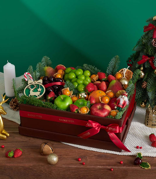 Festive Christmas fruit basket with fresh apples, berries, and candy cane among pine branches and golden ornaments