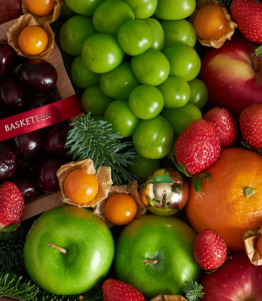 Christmas fruit basket with candy canes, fresh plums, cherries, strawberries, and apples in festive red ribbon gift box