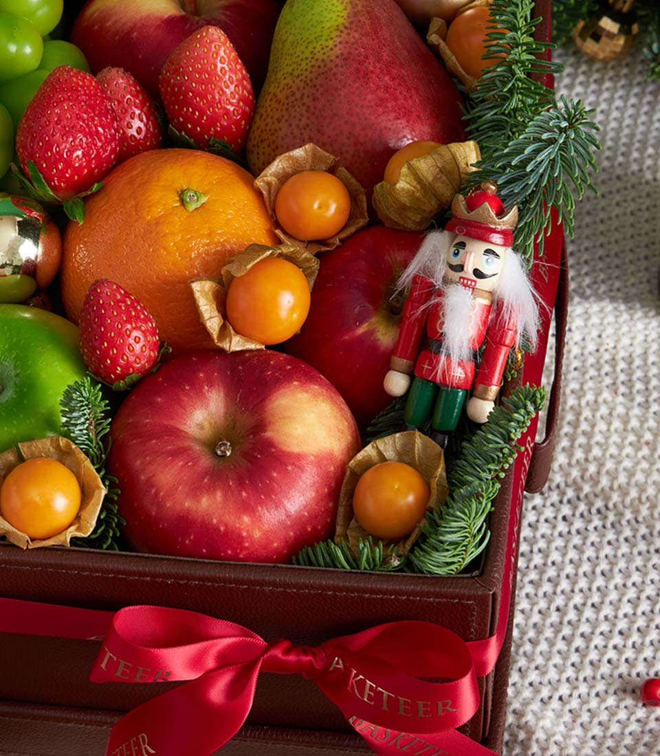 Premium Christmas fruit basket with fresh apples, oranges, grapes and candy canes in luxury brown leather gift box