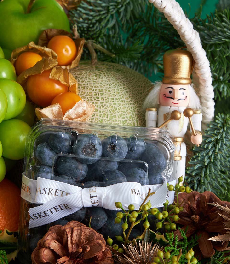 Premium festive fruit basket with blueberries, apples, physalis, and cantaloupe melon, adorned with pine, pinecones, and