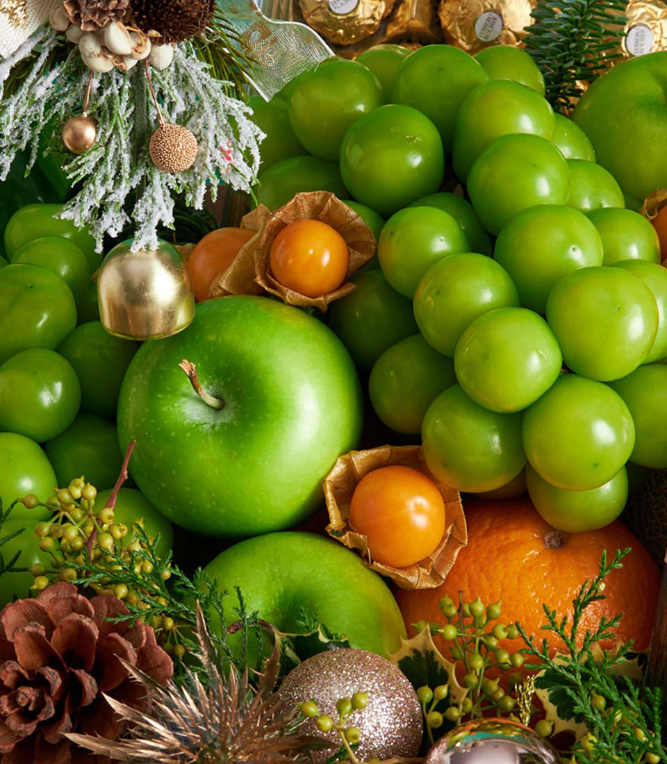 Festive fruit and chocolate gift basket with green apples, tangerines, plums, and goldenberries among gold ornaments and