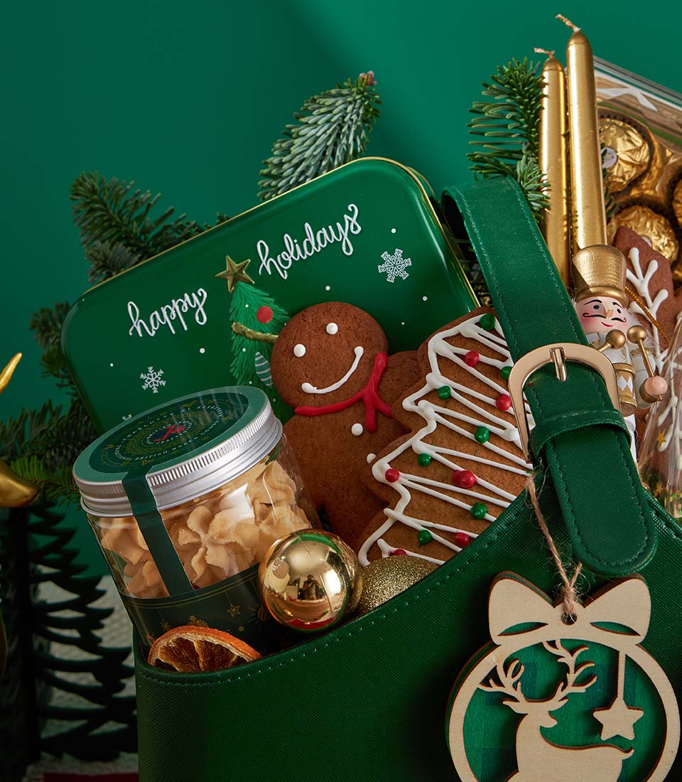 Festive Christmas gift basket with gingerbread cookies, chocolate, golden candles, and holiday ornaments in dark green