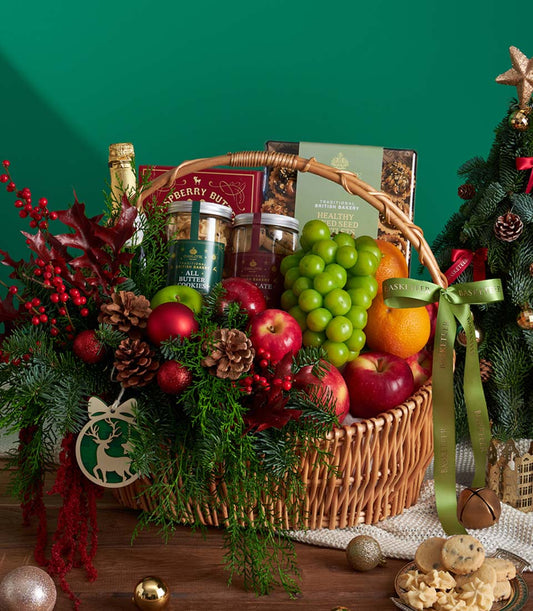 Festive Christmas gift basket with champagne, gourmet cookies, fresh fruits, and pine branches tied with green ribbon