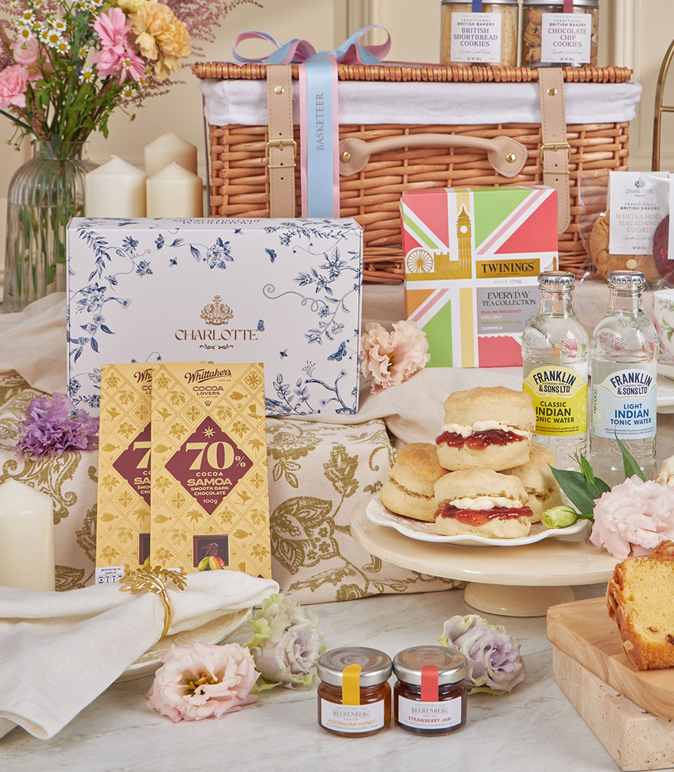 Luxurious afternoon tea hamper with Charlotte pastries, scones, Twinings tea, dark chocolate, and fresh flowers in wicker