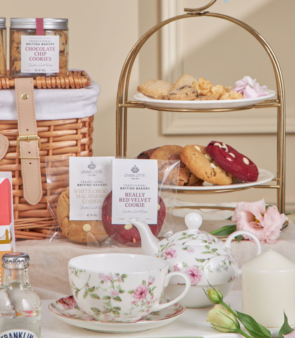 Charlotte Bakery afternoon tea gift set with tiered cookies, floral teacup, and artisan British biscuits in wicker basket