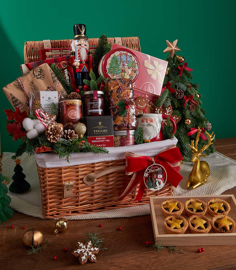 Luxury Christmas hamper with gourmet tea, jam, baked goods, nutcracker and festive mug in wicker basket with red ribbon
