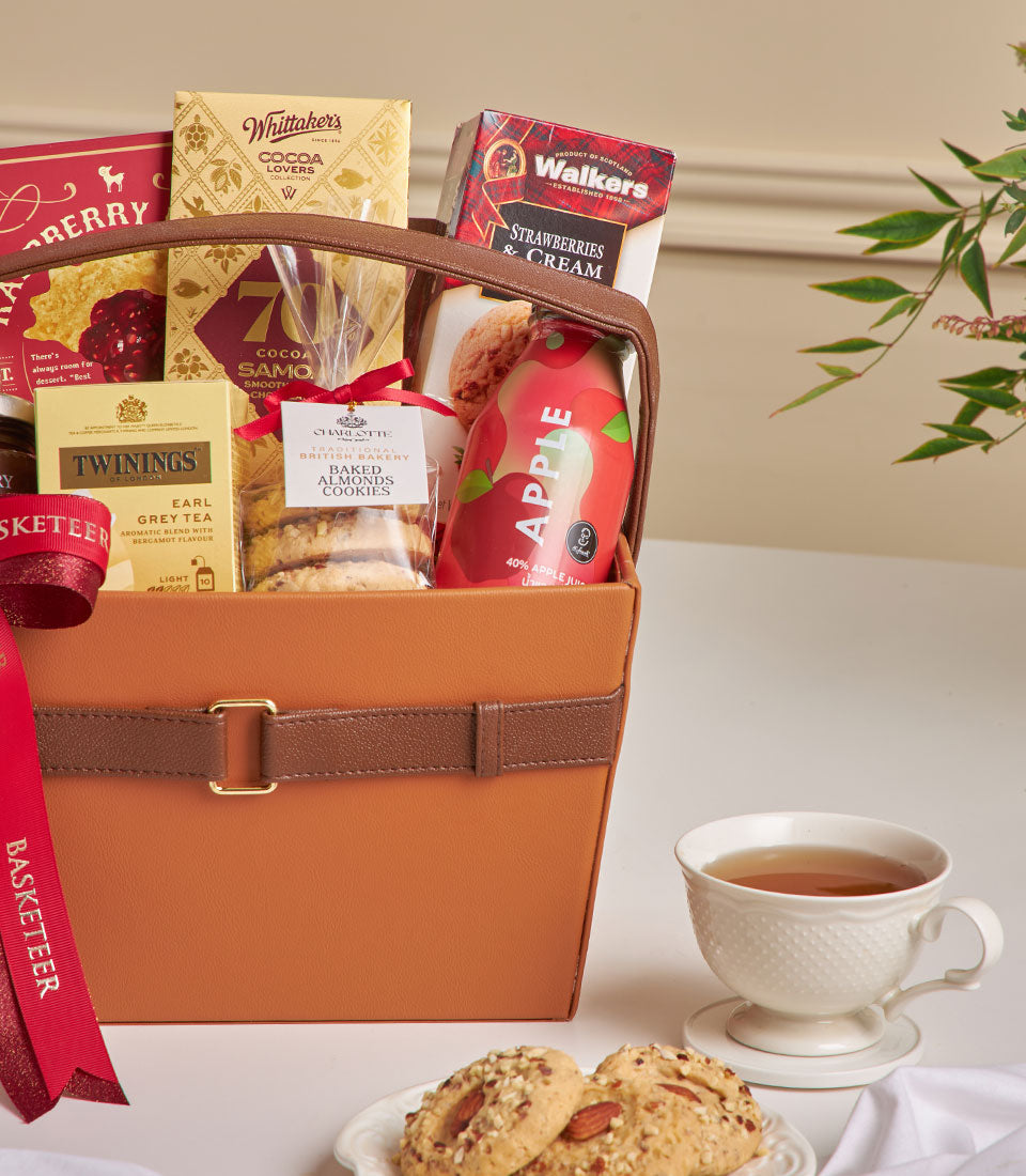 Tan leather gift basket filled with Whittaker's chocolates, Twinings Earl Grey tea, Charlotte bakery cookies, and gourmet