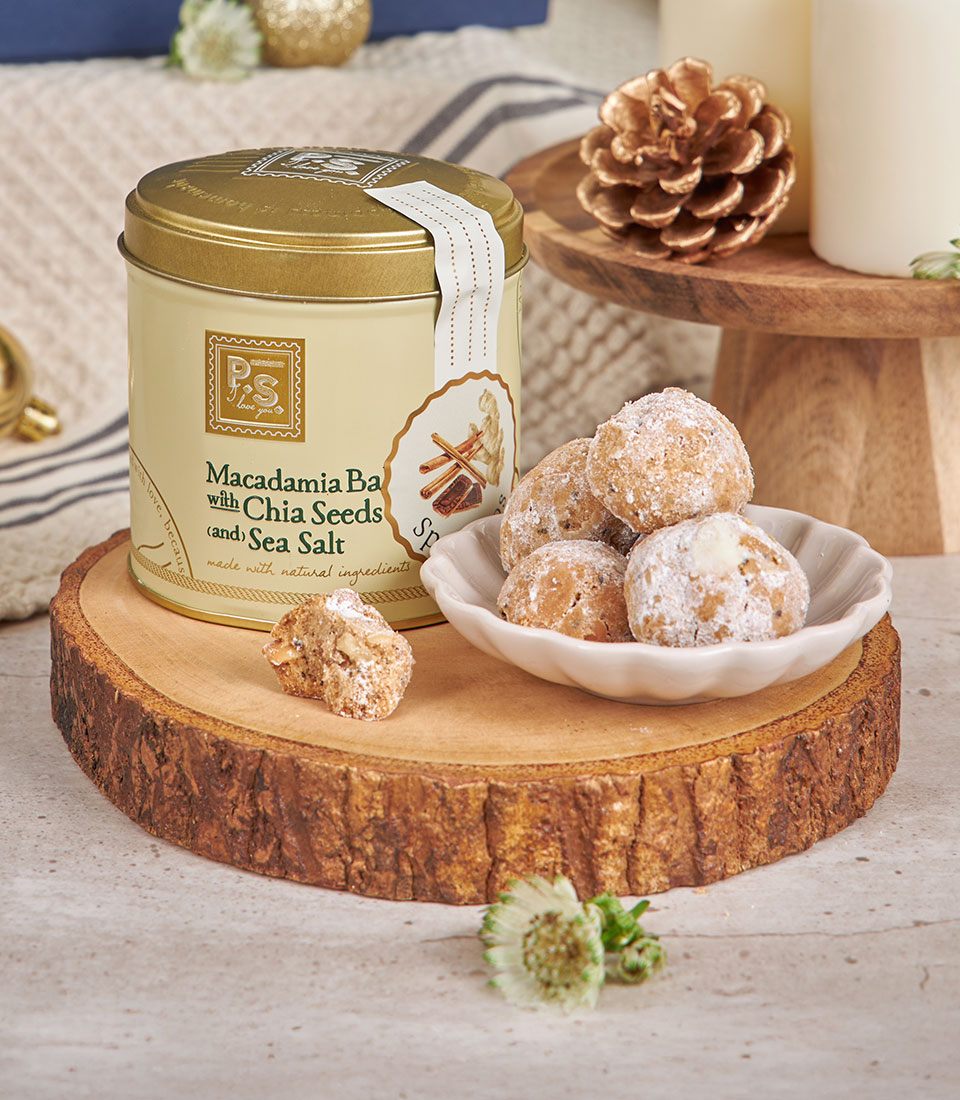 Light yellow macadamia and chia seed cookie tin with powdered sugar dusted rounds on rustic wood, New Year luxury gift hamper