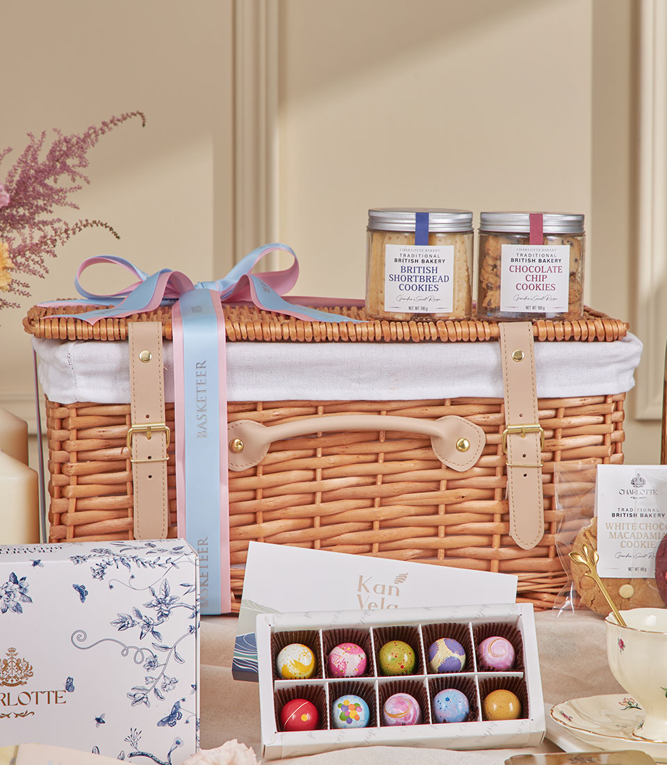 Luxury wicker picnic hamper with British shortbread, chocolate cookies, artisan chocolates, and floral tea cup for afternoon