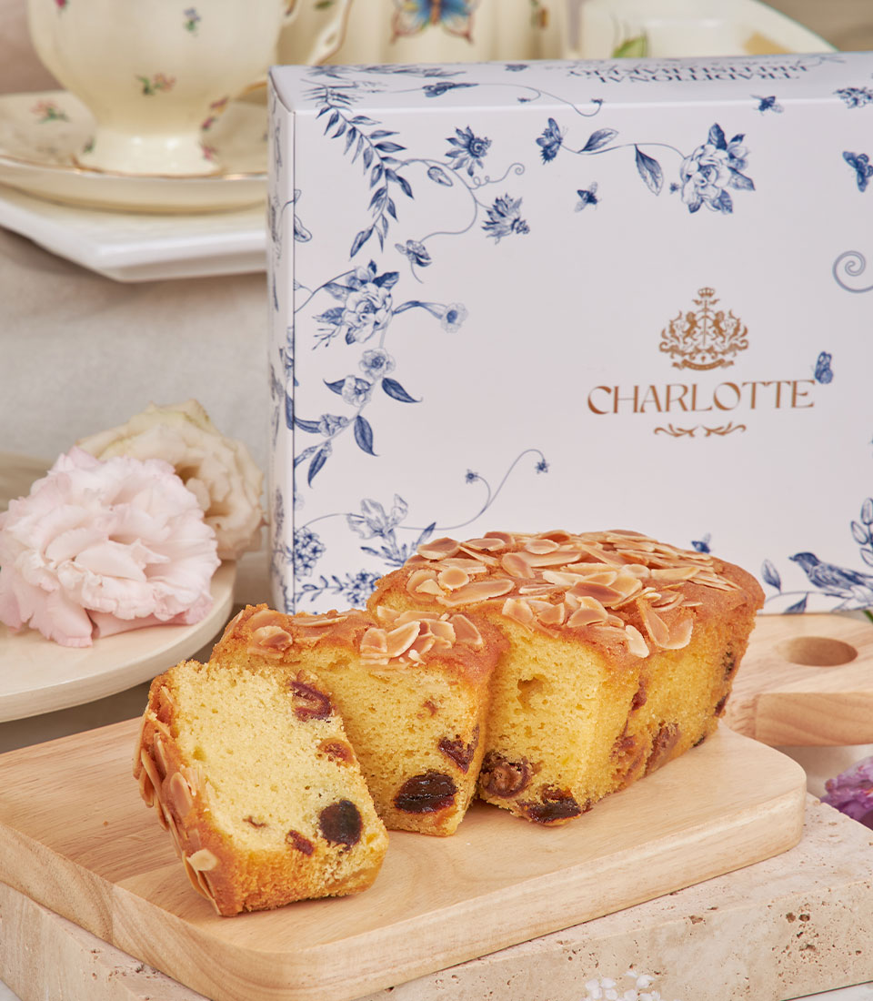 Golden fruit cake with almonds and dried fruits beside Charlotte Bakery afternoon tea gift box, teacups, and fresh flowers