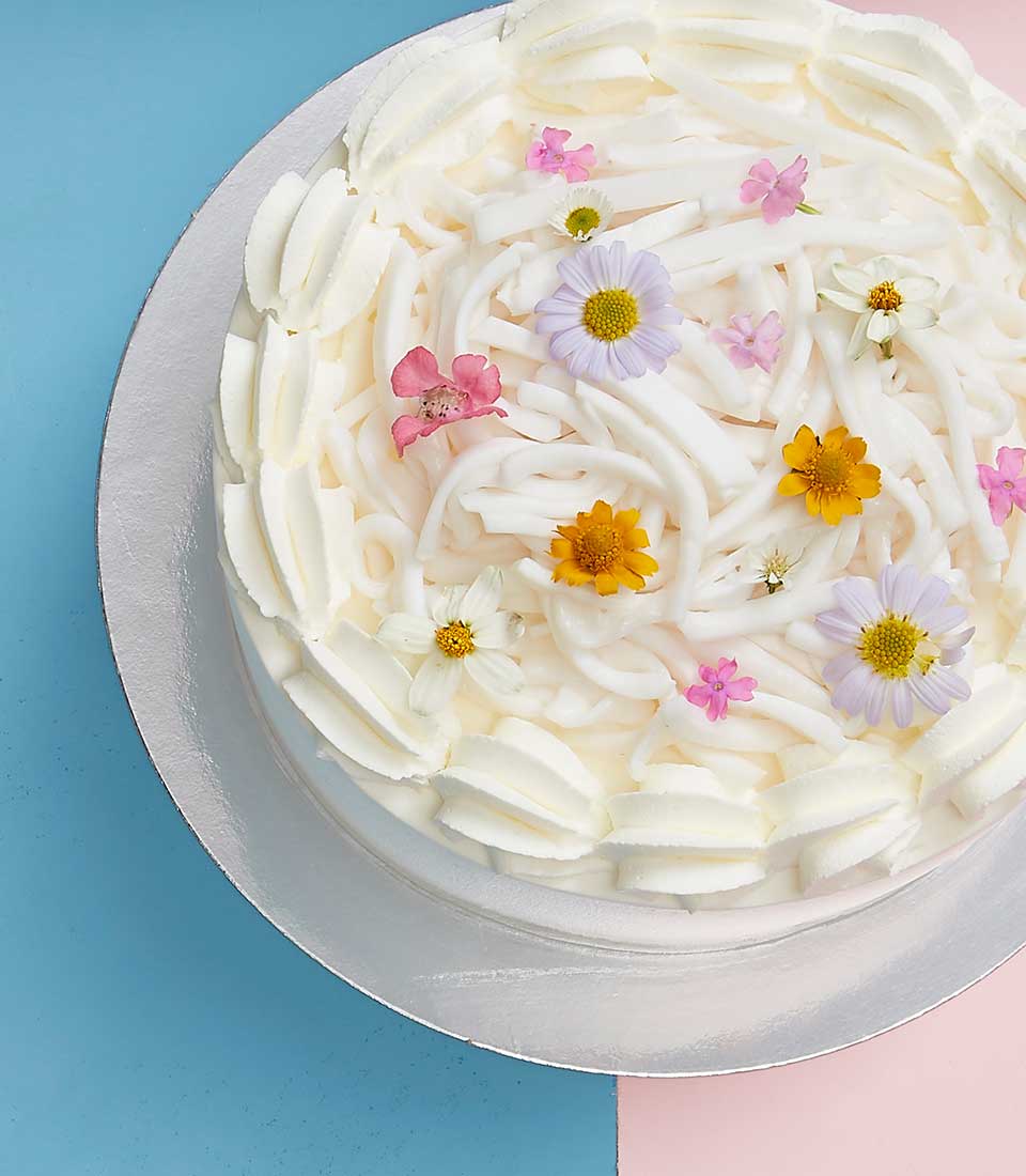 Tender coconut Mother's Cake with white cream frosting, fresh flowers, and coconut noodles on silver board