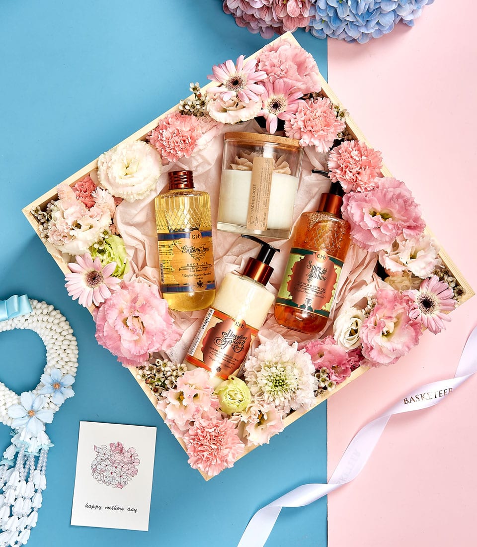 Wooden spa gift box with garden rose candle, body oil, lotion, and shower gel surrounded by pink and white flowers
