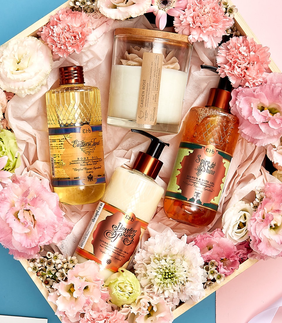 Luxury spa gift set with body oil, gel cream, and rose candle nestled in pink roses and white flowers