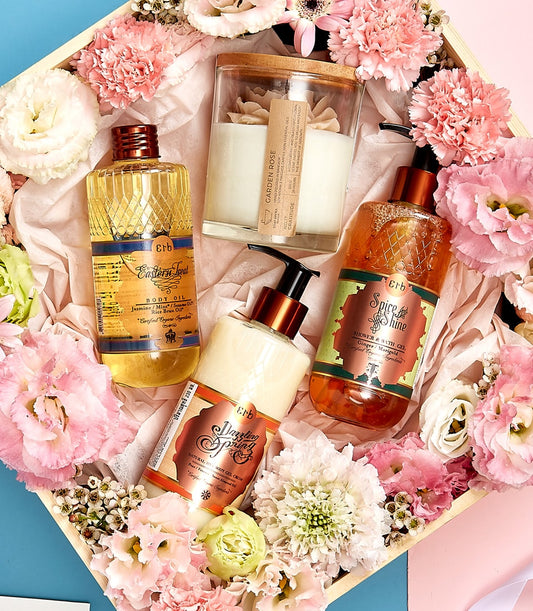Luxury spa gift set with body oil, gel cream, and rose candle nestled in pink roses and white flowers