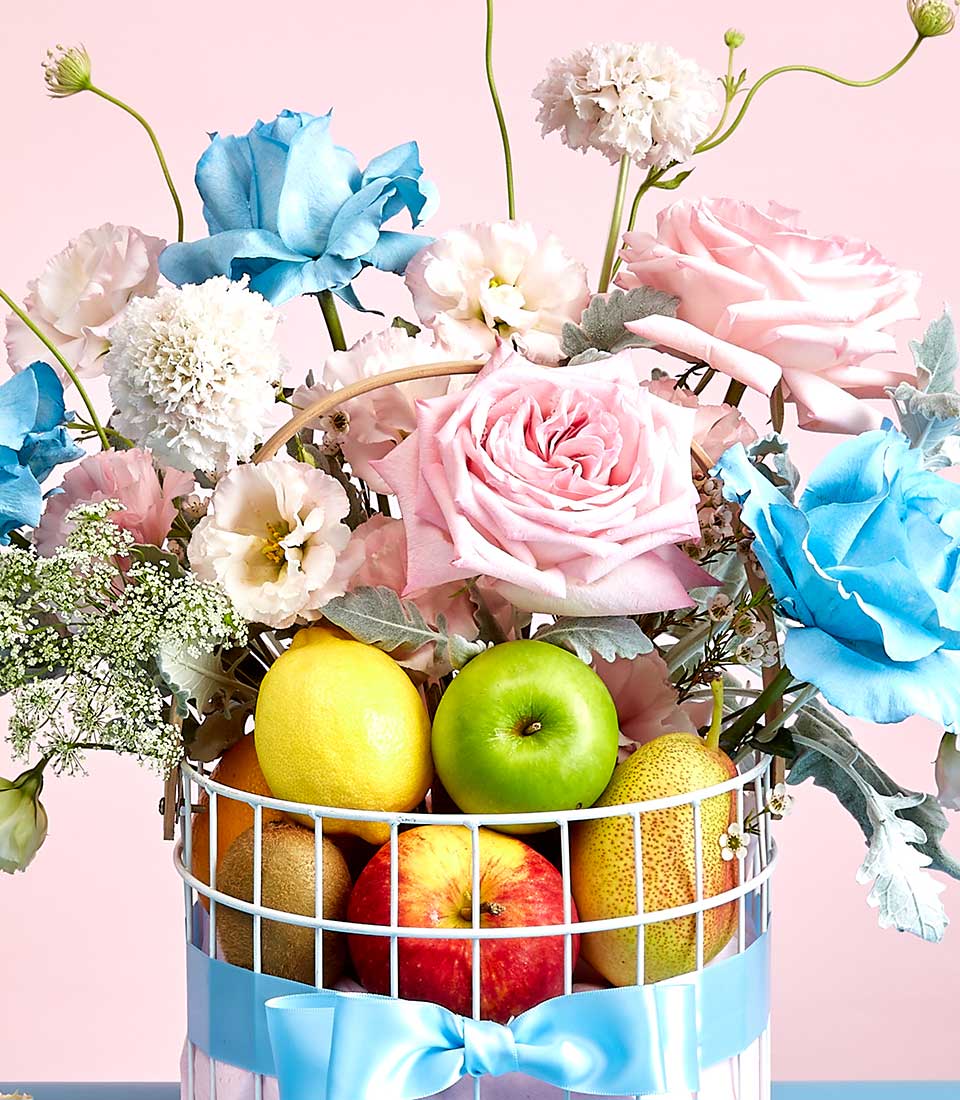 Fresh flowers and gourmet fruits in white wire basket, Mother's Day gift with roses and seasonal produce