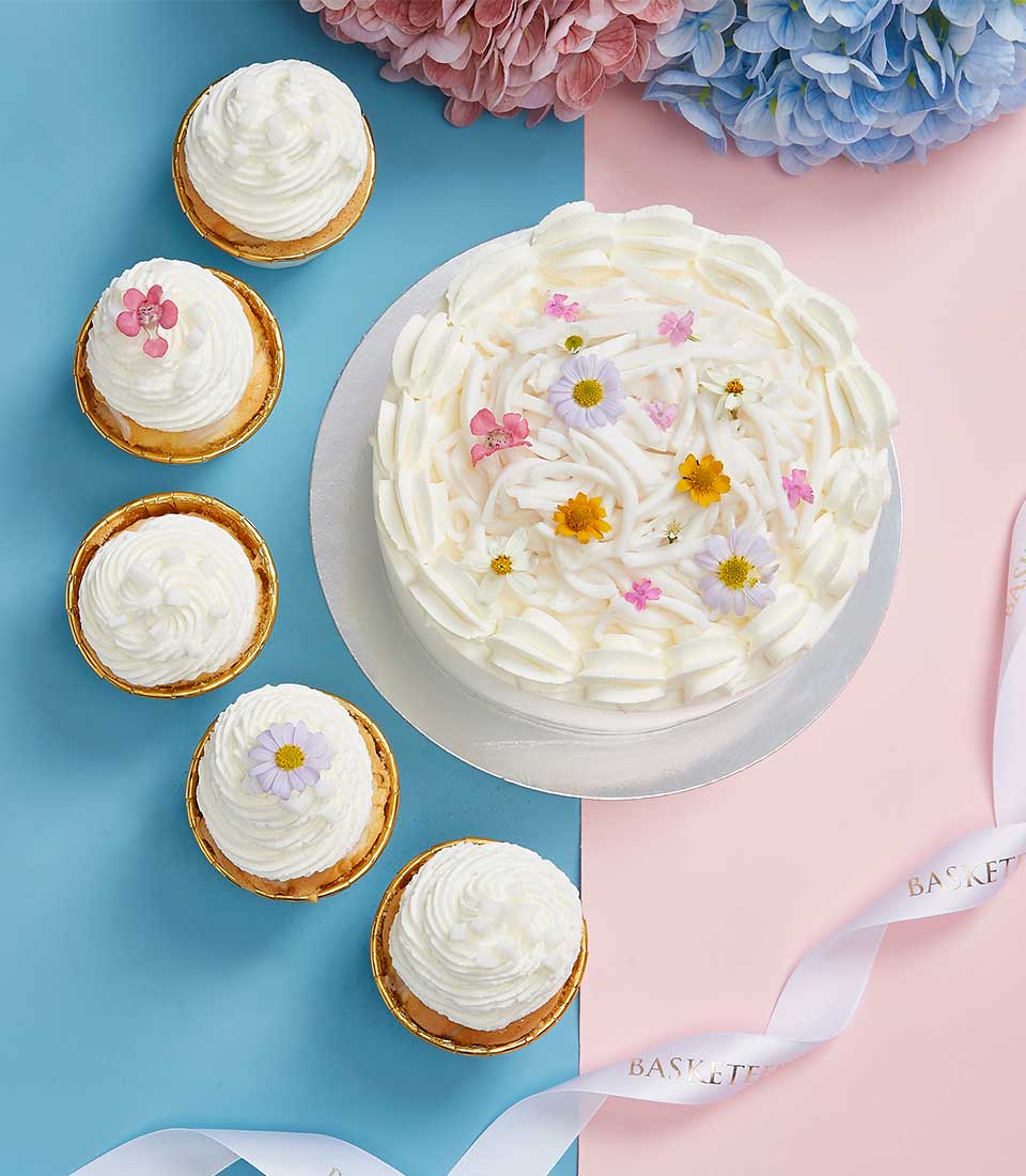 White cream frosted coconut cake with colorful flowers and five gold-lined cupcakes for Mother's Day celebration
