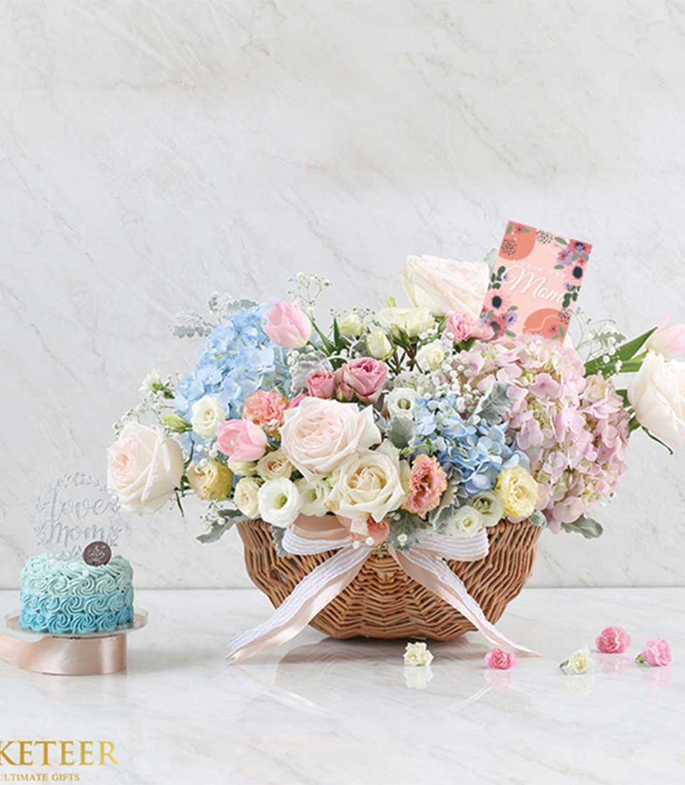Wicker basket of fresh roses, hydrangeas, and tulips with sky blue ombre Mother's Day cake on marble stand