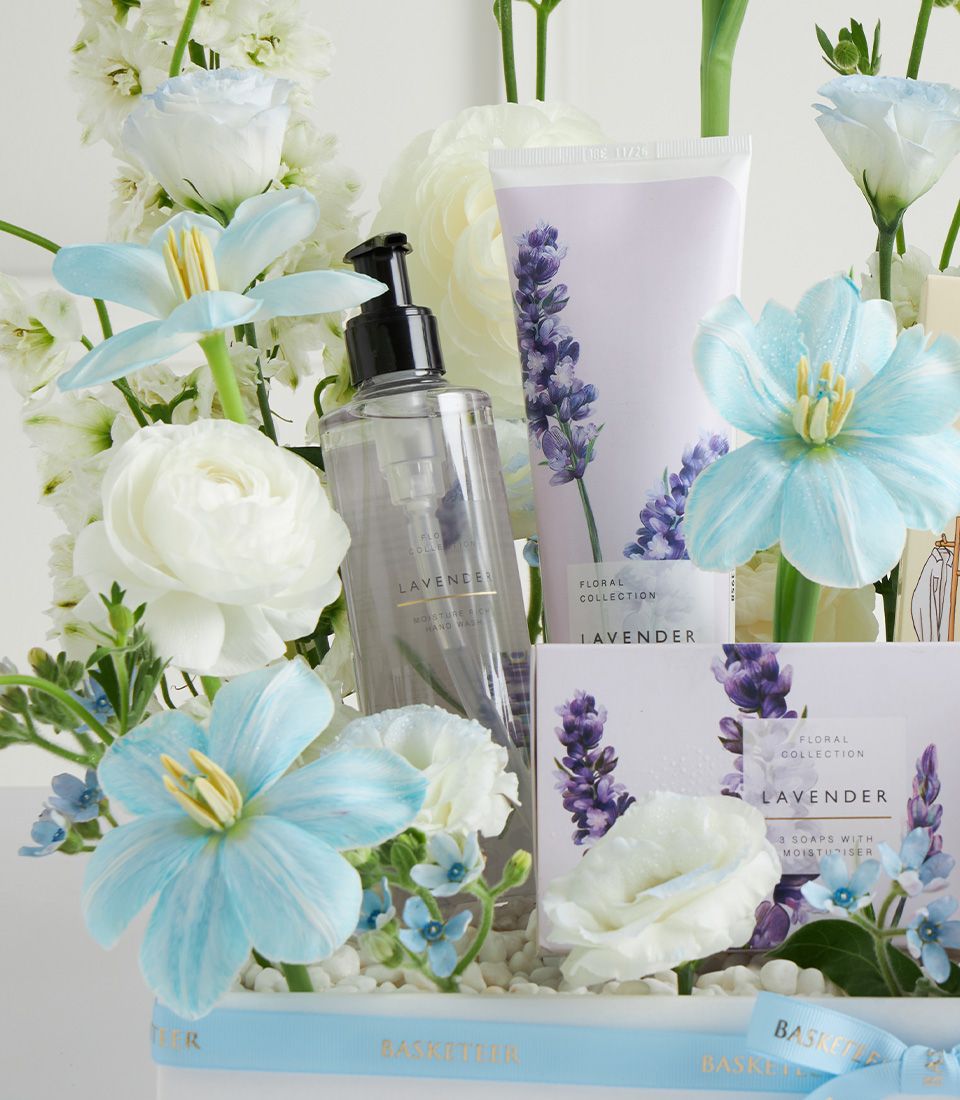 Lavender spa gift basket with hand wash, lotion, and soaps surrounded by white and blue flowers