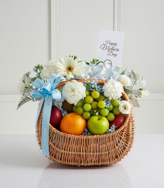 Wicker basket with fresh fruit, white gerberas, blue hydrangeas, and ranunculus for Mother's Day