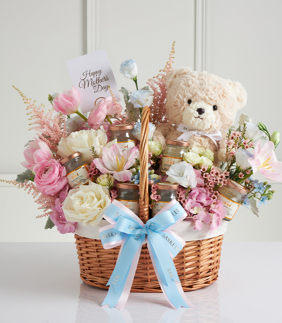 Wicker gift basket with pink and white roses, hydrangeas, bird's nest jars, and cream teddy bear for Mother's Day