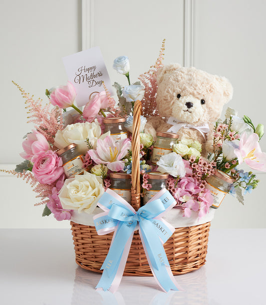 Wicker gift basket with pink and white roses, hydrangeas, bird's nest jars, and cream teddy bear for Mother's Day