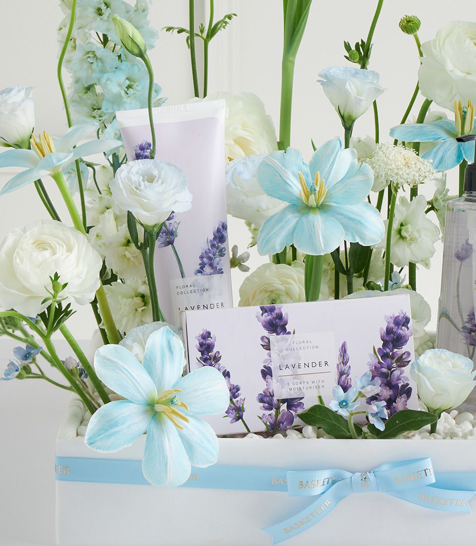 Luxury lavender spa basket with fresh white ranunculus, light blue tulips, and artisan bath products for Mother's Day