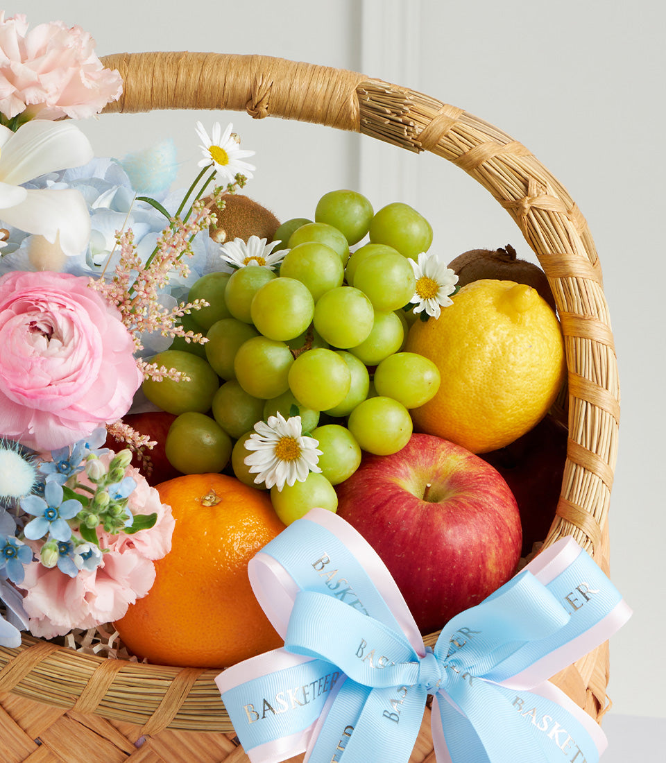 Pastel Mother's Day fruit basket with fresh grapes, apple, citrus, and pink ranunculus in woven wicker