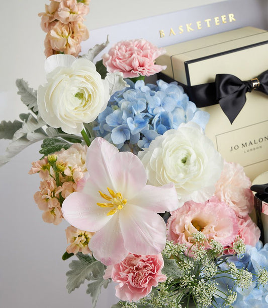 Luxe pastel flower arrangement with white ranunculus, pink tulips, and hydrangeas alongside Jo Malone candle gift box
