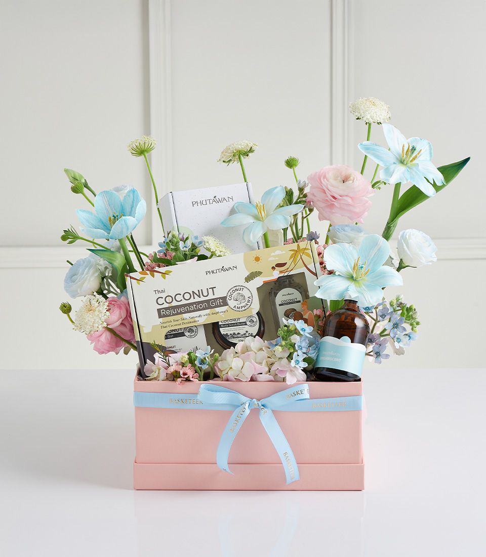Pastel spa gift box with Thai coconut skincare, PHUTAWAN products, amber bottle, and fresh tulips, ranunculus in soft pink