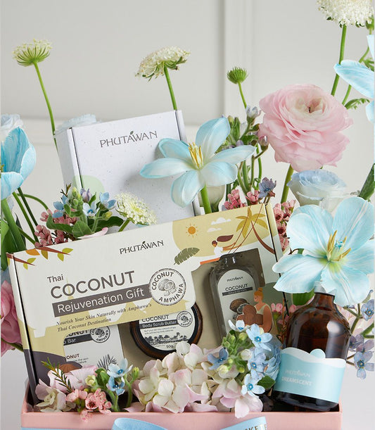 Pastel spa gift box with coconut body scrub, natural oil, and soap surrounded by pink, blue, and white flowers for Mother's
