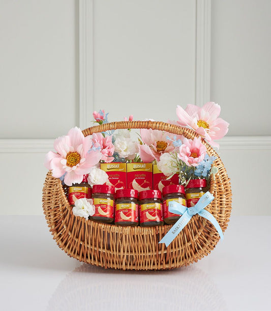Classic bird's nest gift basket with wicker weave, red-capped jars, and pink-white-blue artificial flowers for Mother's Day