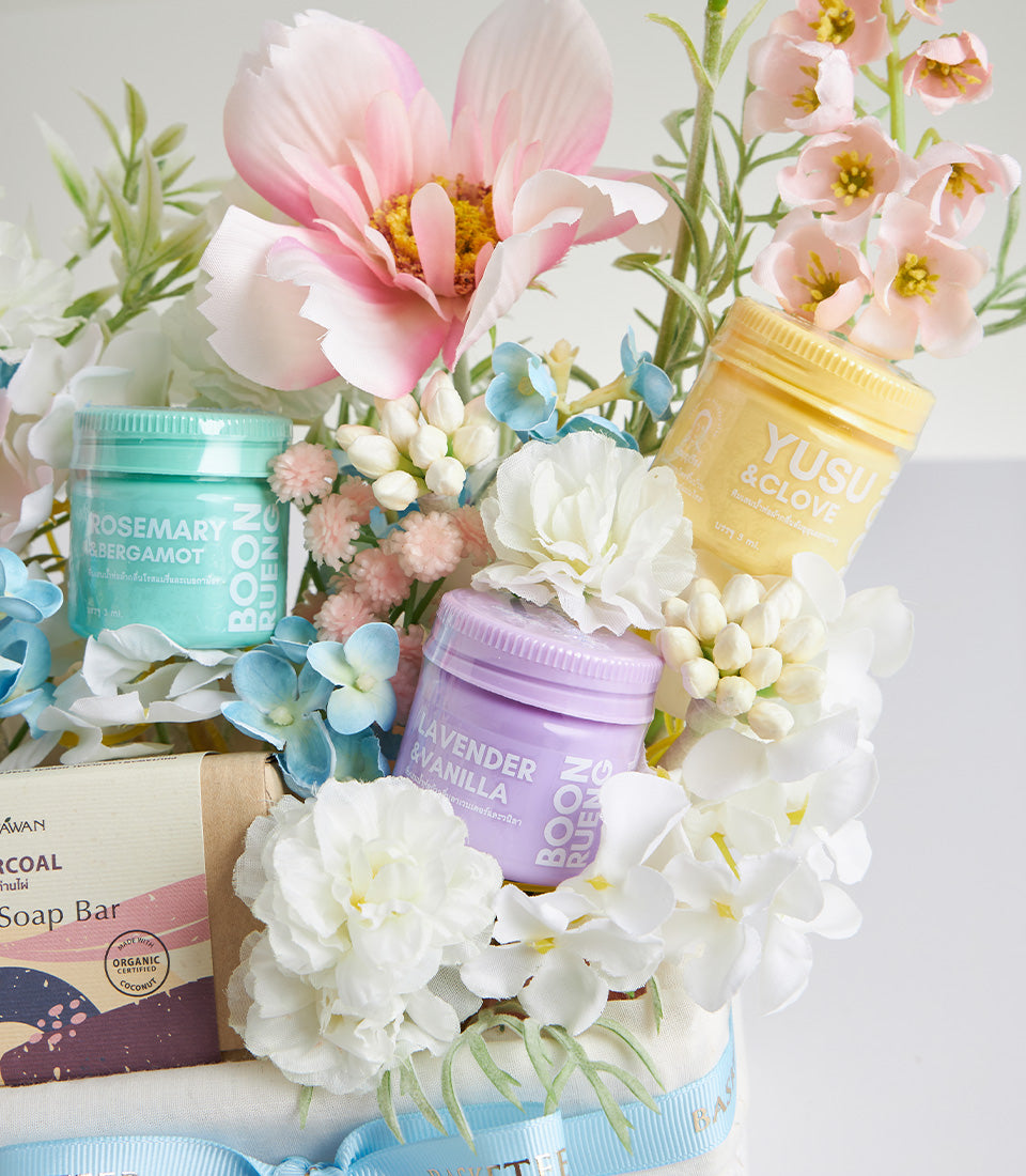 Herbal spa gift basket with rosemary bergamot, yuzu clove, and lavender vanilla bath products among pink and white flowers