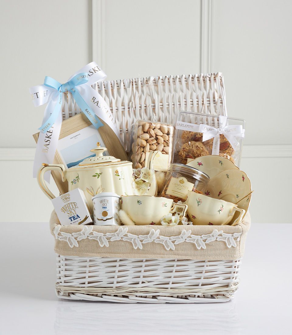 Luxury white wicker gift basket with cream floral teapot, teacups, gourmet teas, pistachios, and preserves for Mother's Day
