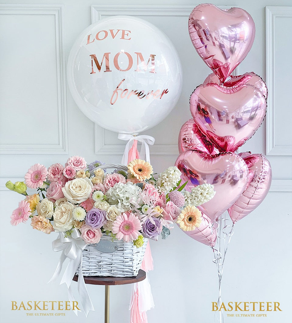 White woven flower basket with pastel roses, gerberas, hydrangeas and hyacinths, paired with love-themed balloons for