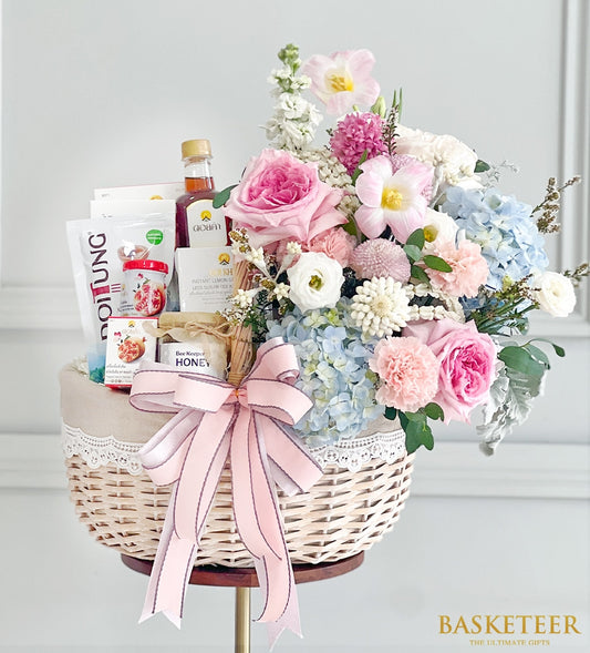 Woven wicker gift basket with Doi Tung and Doi Kham gourmet selections, fresh pink roses, white ranunculus, and hydrangeas