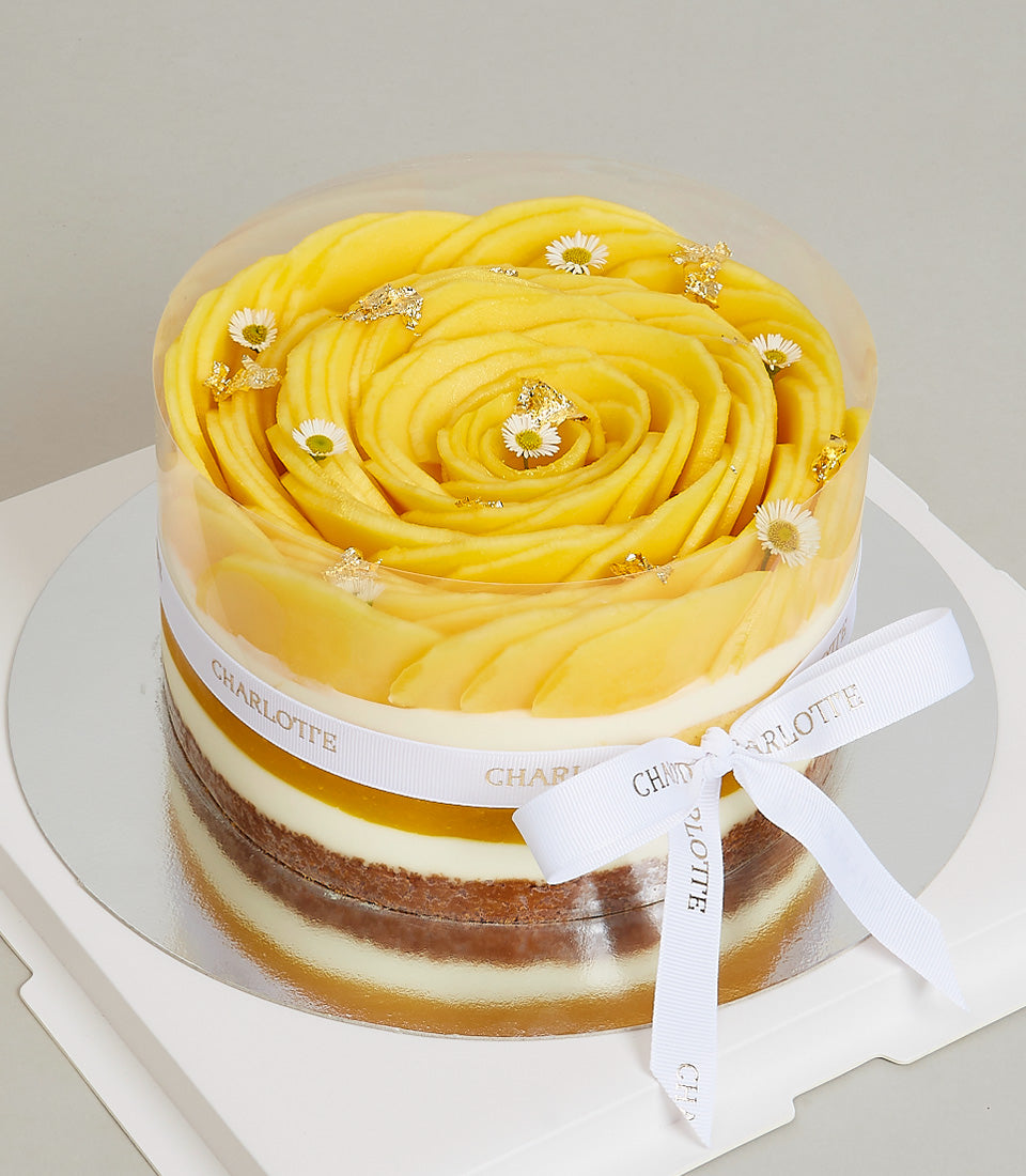 Exotic mango layer cake with spiral fresh mango, cream layers, and gold leaf in clear gift box