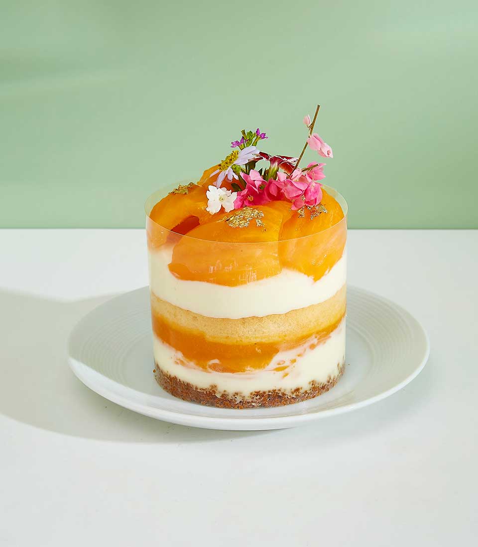 Mini But Mighty Mayongchid Layer Cake in clear cylinder with cream, tropical fruit, and edible flowers