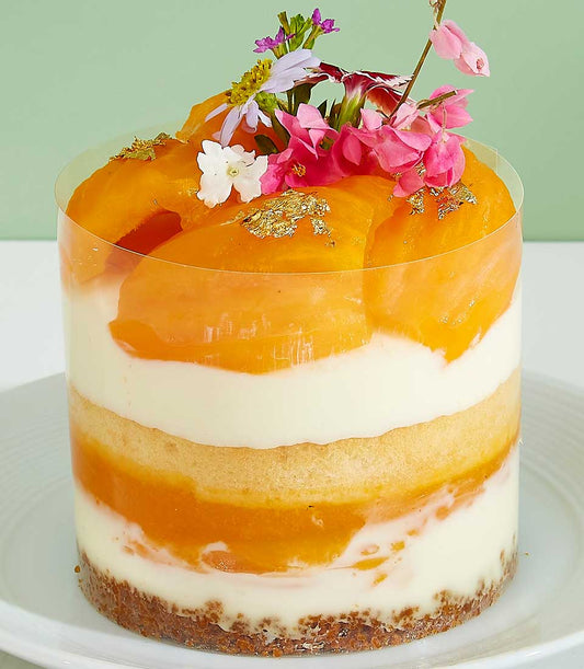 Mini Mayongchid layer cake with peach, cream mousse, and edible flowers in clear container