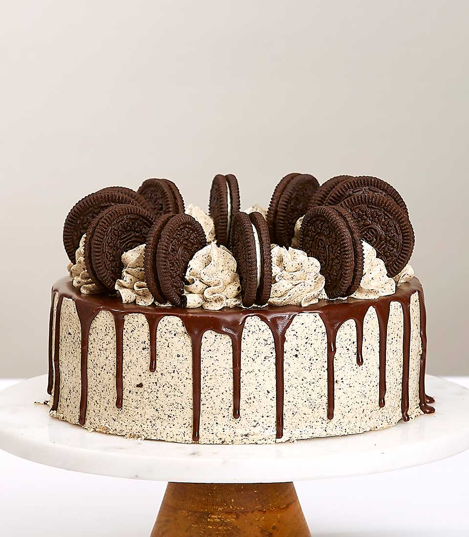 Oreo chocolate cream layer cake with ganache drip and cookie toppings on marble stand