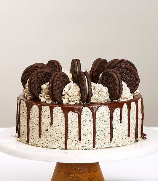 Oreo chocolate cream layer cake with ganache drip and cookie toppings on marble stand