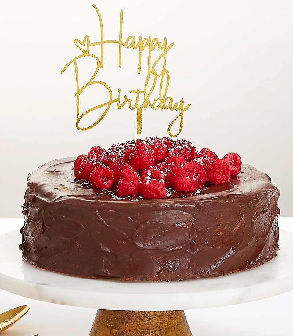 Dark chocolate ganache layer cake with fresh raspberries and gold birthday topper on marble stand