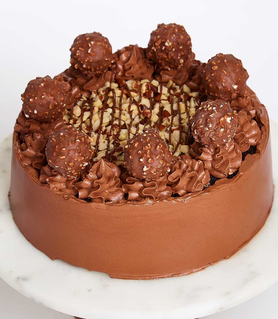 Round chocolate cake with hazelnut Ferrero Rocher, piped frosting swirls, and dark chocolate drizzle on marble stand