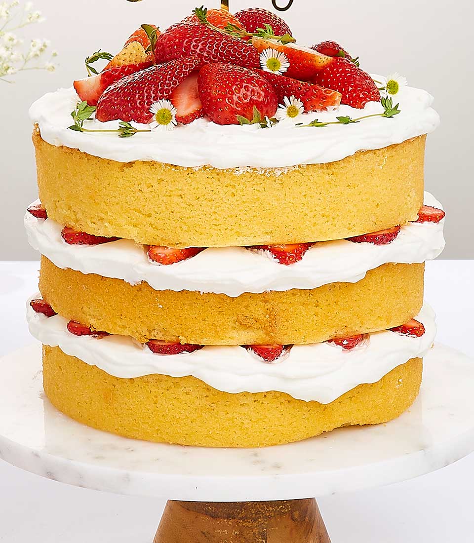 Triple-layer strawberry shortcake with whipped cream and fresh berries on marble stand