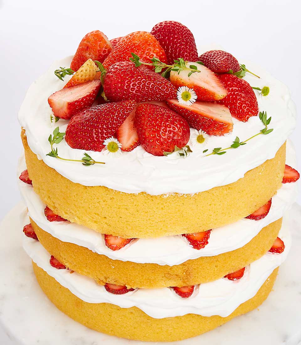 Triple-layer strawberry shortcake with whipped cream, fresh berries, and edible flowers on marble stand