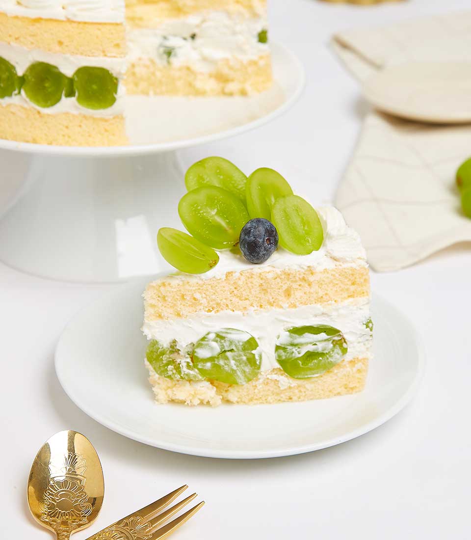 Light yellow sponge cake layered with white cream, fresh green grapes, and blueberries for celebration
