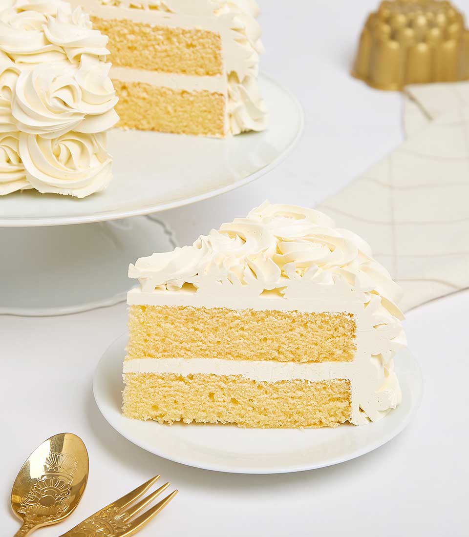 Creamy Indulgence vanilla layer cake with white buttercream rosettes, presented on cake stand with slice displayed