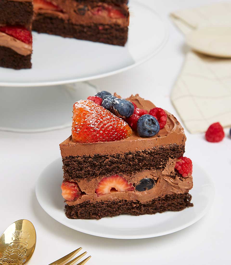 Chocolate cake slice layered with strawberries and blueberries, topped with fresh berries and powdered sugar