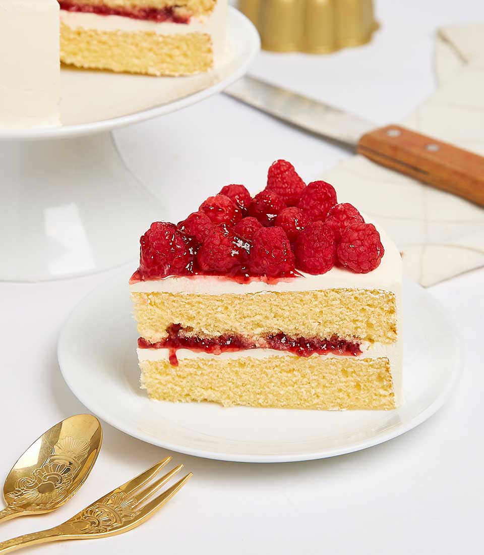 Raspberry layer cake with fresh berries and glaze, artisan birthday cake slice on white plate