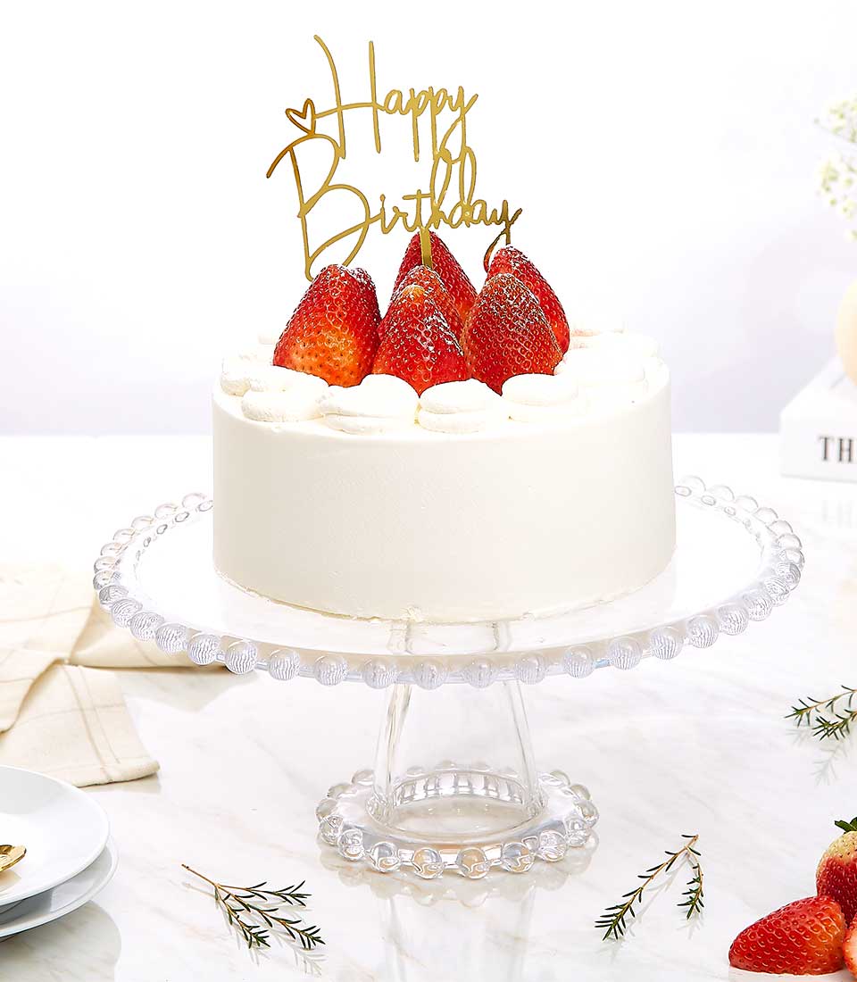 Whipped strawberry layer cake with fresh berries and gold Happy Birthday topper on beaded glass stand